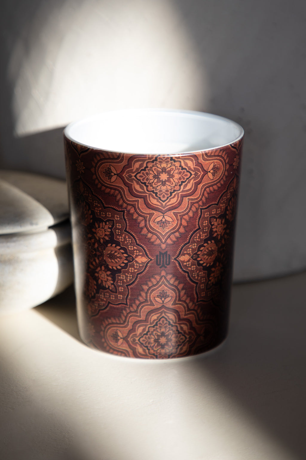 Close-up of a deep brown luxury candle with intricate Arabesque pattern by Muriḥ in dramatic lighting